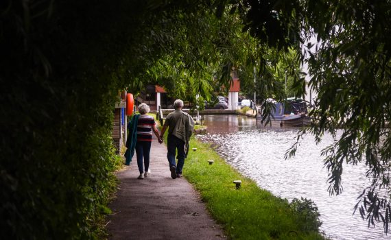 senior couple walking along lake embankment holding hands