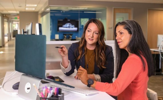 two women sitting at a table looking at a computer screen